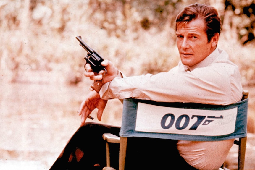 Roger Moore on set holding a gun, playing James Bond in 1972.
