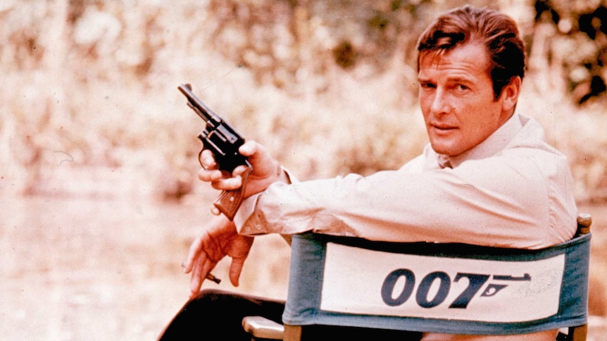 Roger Moore on set holding a gun, playing James Bond in 1972.