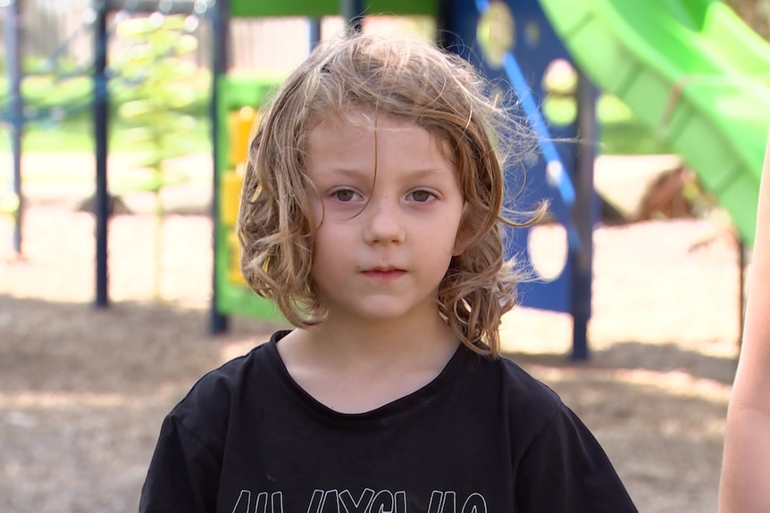A boy with long hair in front of a playground