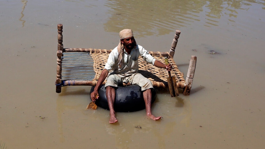 A displaced man carries belongings he salvaged from his flood-hit home as he paddles through a flooded area.