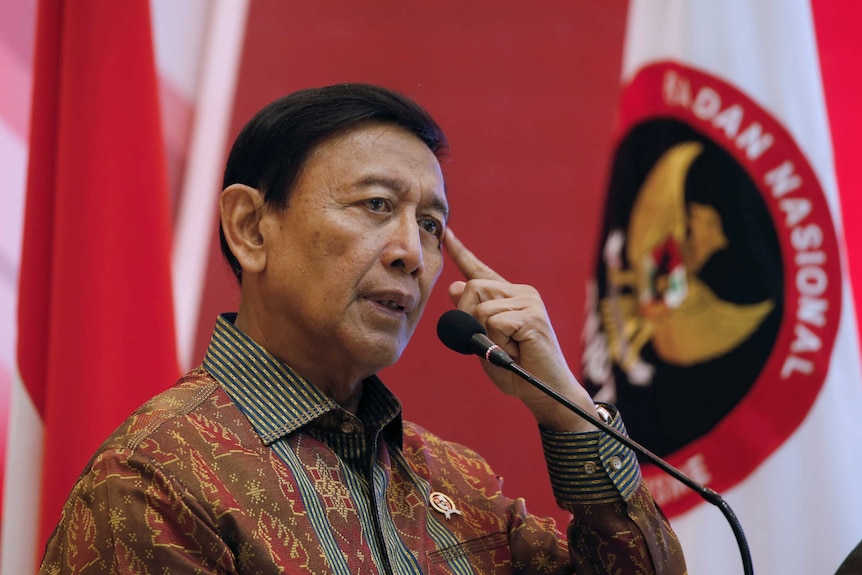 Wiranto, standing in front of an Indonesian flag, points to his head.