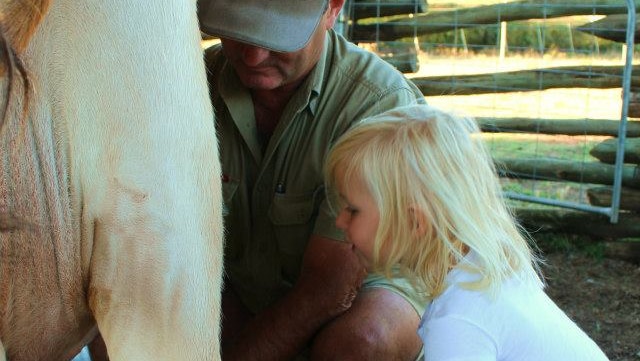 Tasmanian farmer Rowen Carter showing a young girl how to milk a cow.