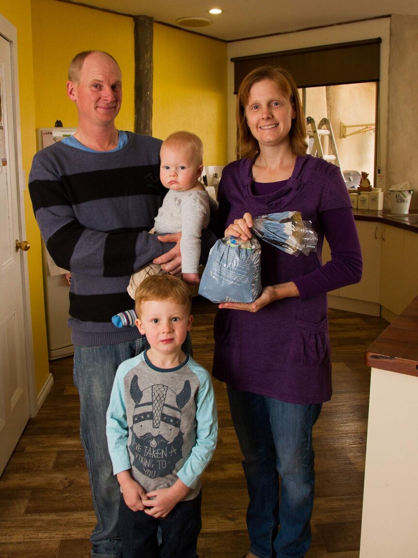 A family stand in their kitchen holding a plastic bread bag