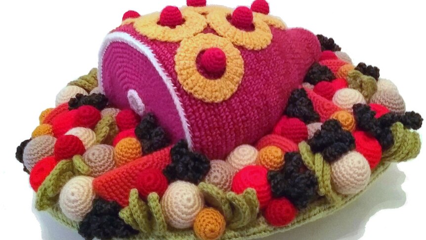 A crocheted leg of ham with pineapple on top, surrounded by crocheted vegetables.