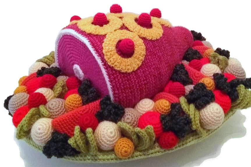 A crocheted leg of ham with pineapple on top, surrounded by crocheted vegetables.