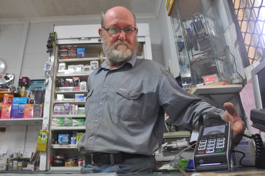 Owner of a petrol station in Batchelor stands over his desk looking at the EFTPOS machine.