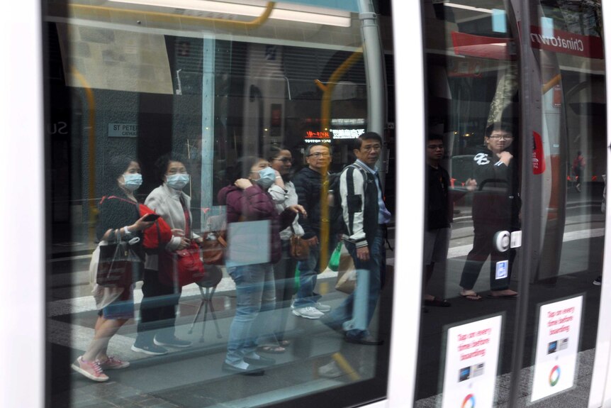 A group of people in the reflection of a light rail car's window, some are wearing face masks.