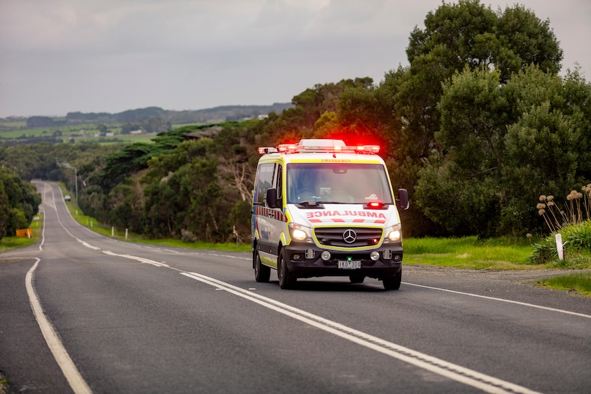 Ambulance driving with flashing lights on long empty country road