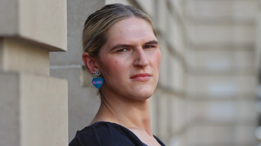 a woman wearing glittering earrings with 'queer' written on them