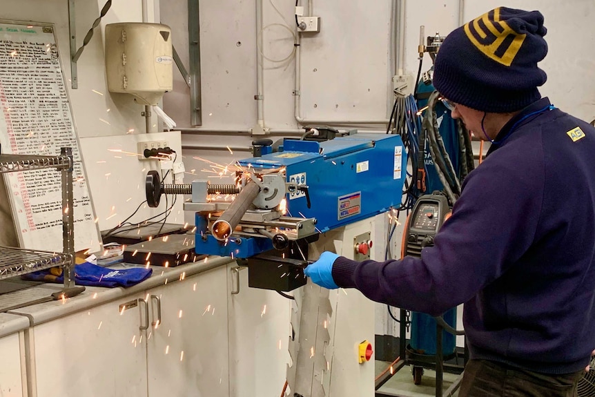 A worker machines a metal tube with sparks flying.