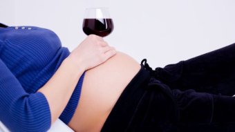 A pregnant woman is lying on her back holding a glass of red wine over her round belly.