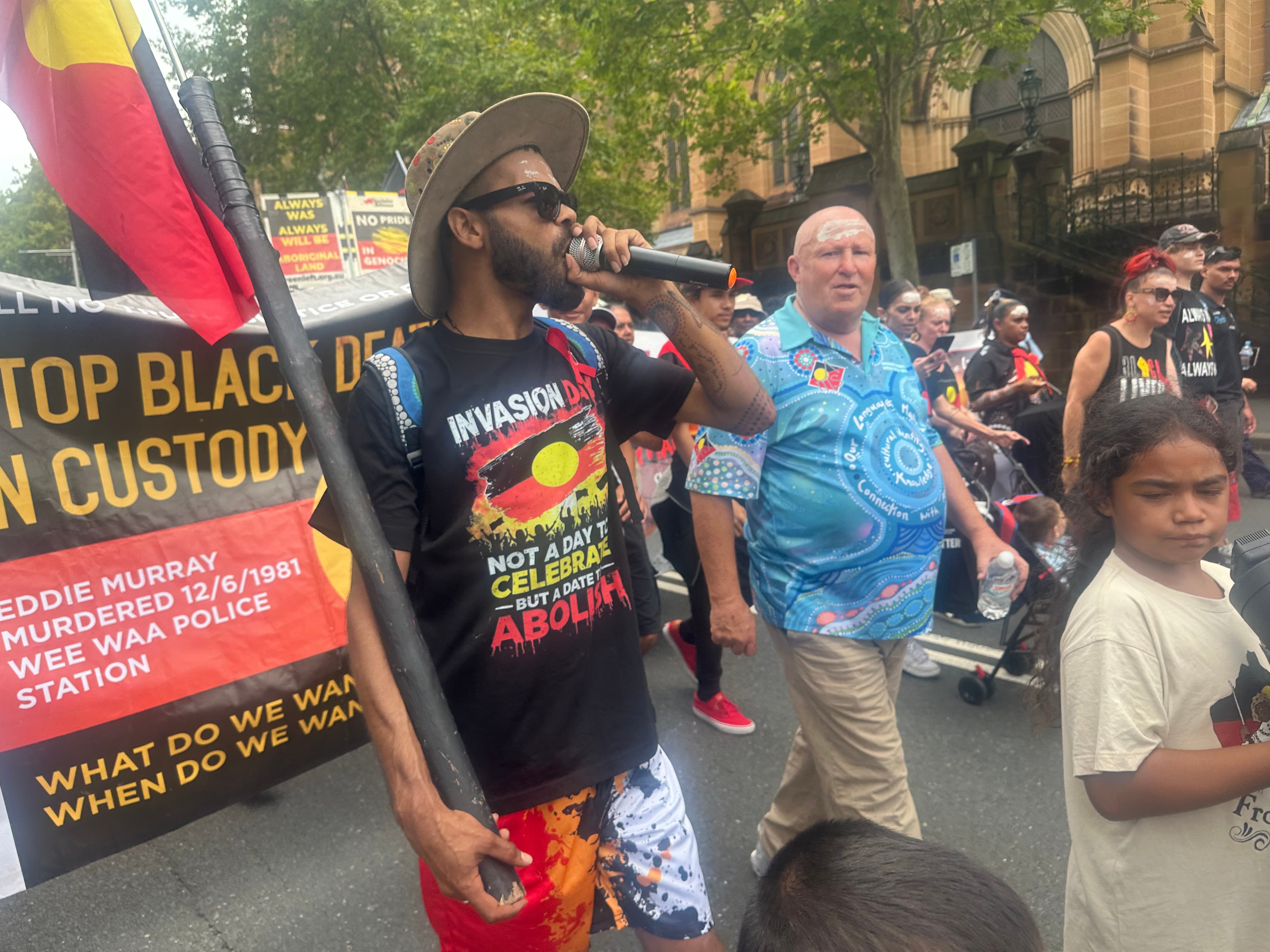 Um homem com um microfone carregando uma bandeira aborígene.