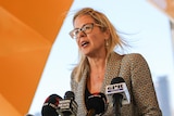 A mid shot of Libby Mettam speaking at a media conference indoors in front of microphones.