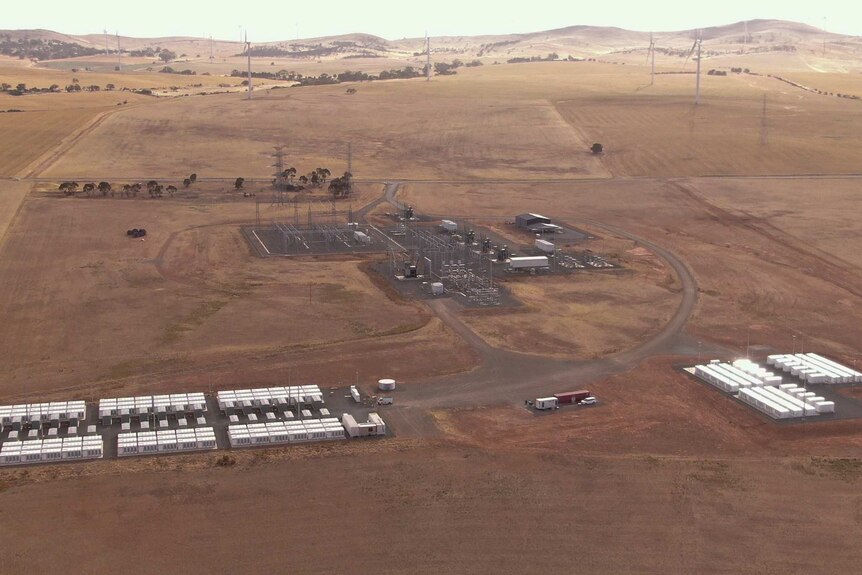 Aerial photo showing the Hornsdale battery in the foreground with wind farms in the background. The ground is brown.