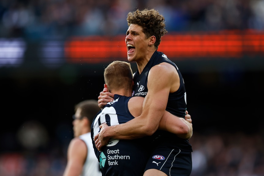 Two Carlton AFL players embrace as they celebrate a goal.