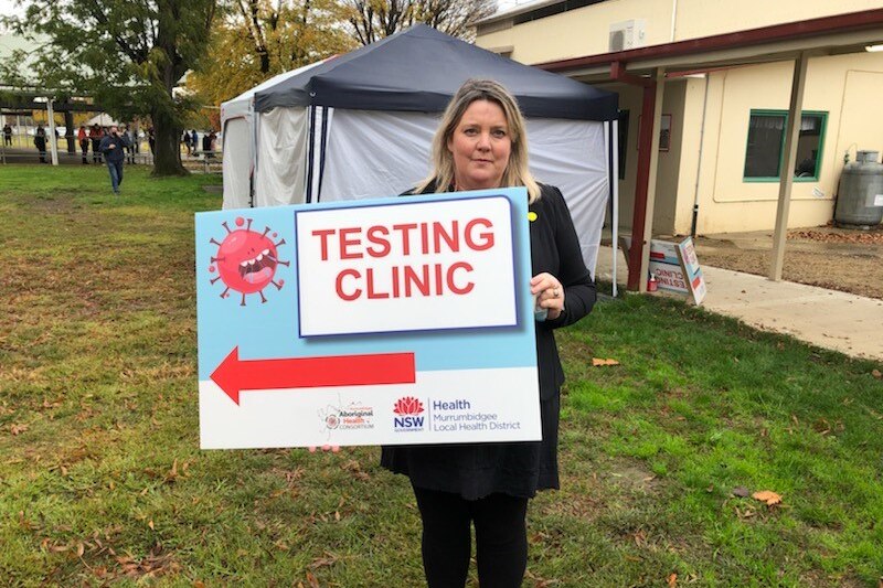 Woman wearing a black coat holding a sign 'testing clinic'