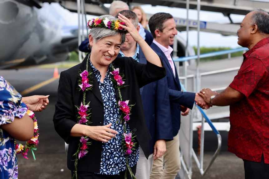 An Asian woman smiling, wearing a flower crown and lei over formal clothing