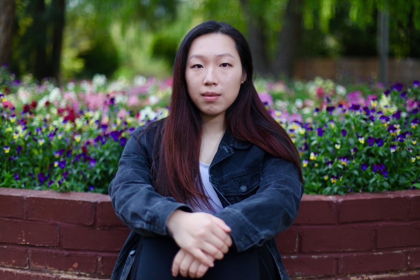 Annie Wange sits in front of a flower bed.