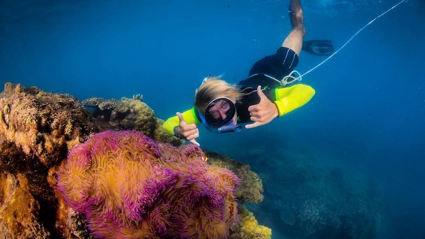 A man poses with underwater with a colourful sea plant.