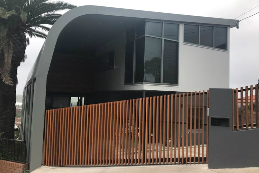 The front of a house with the number with a timber gate out front.