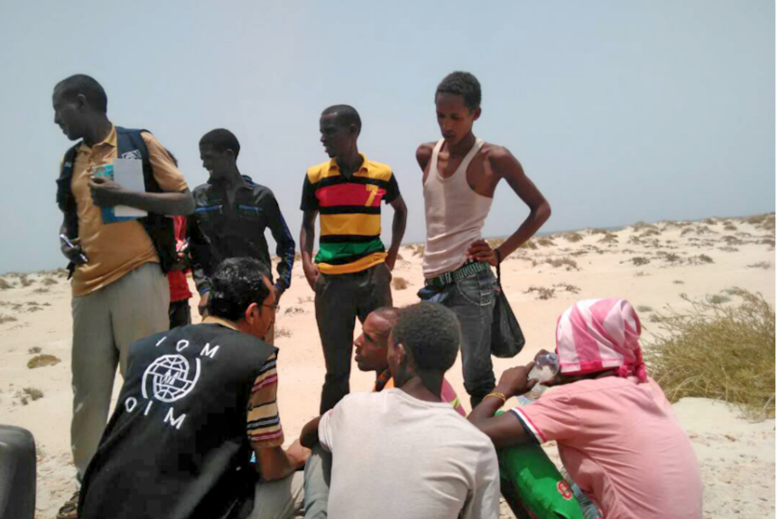 An aid worker stands on a Yemen beach with a handful of migrants.