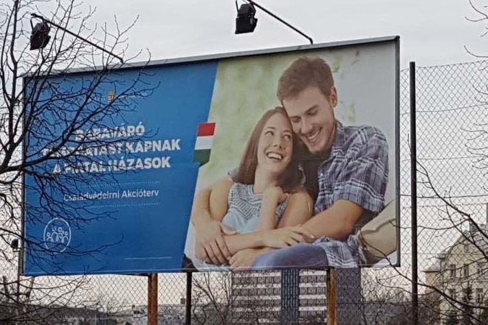 A billboard featuring a man and a woman cuddling together on a couch. The slogan is written in Hungarian.