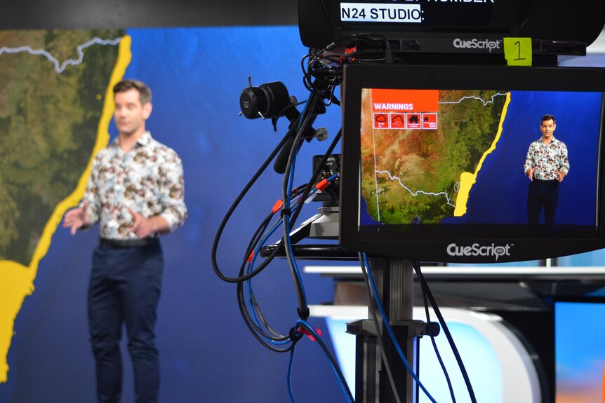 Camera filming man standing in front of weather maps in a TV studio.