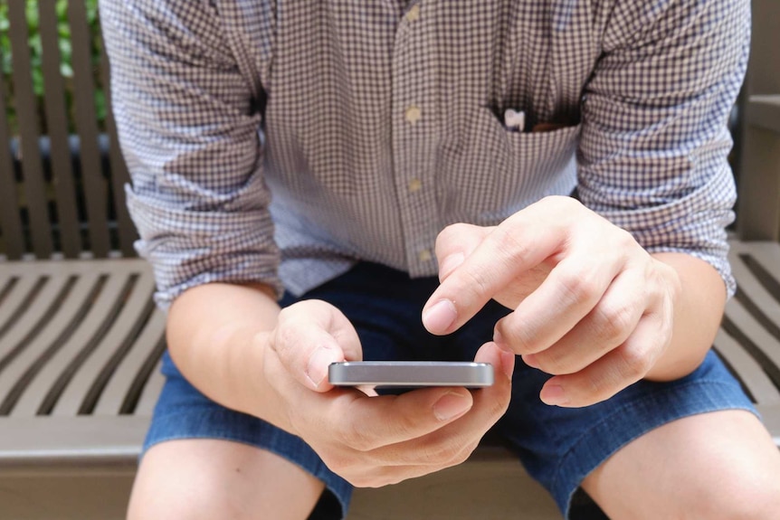 A man sitting on a bench using a mobile phone with his head out of shot