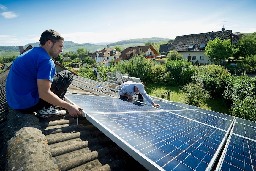 Two men installing solar panels on a roof.