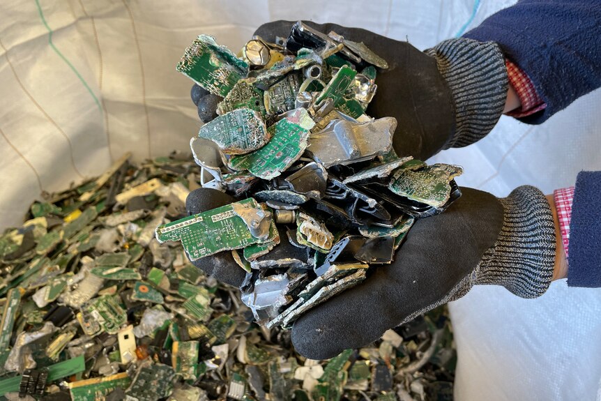 mans gloved hands hold bits of green circuit boards 