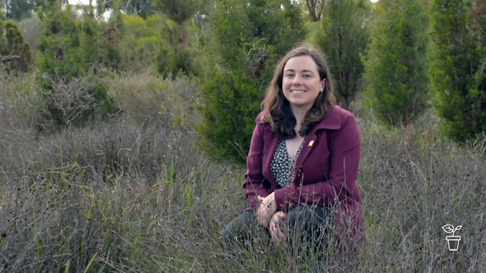 Young woman sitting in the bush, smiling at the camera