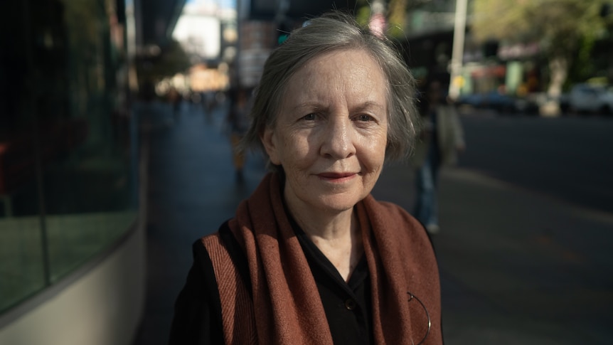 A woman standing outside on a footpath, smiling.