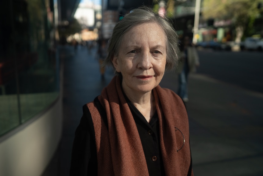 A woman standing outside on a footpath, smiling.