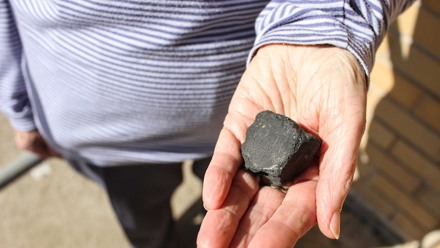 A woman's hand holding a piece of meteorite that looks like a black rock.
