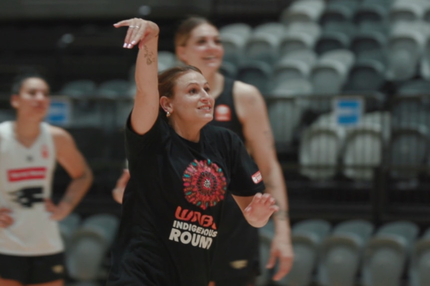 Tiana Mangakahia wears a black t-shirt and has one arm up in the air, after she has taken a shot at the basket.