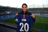 Sam Kerr holds up a Chelsea soccer jersey in the stands of Stamford Bridge