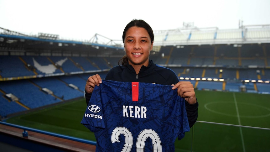Sam Kerr holds up a Chelsea soccer jersey in the stands of Stamford Bridge