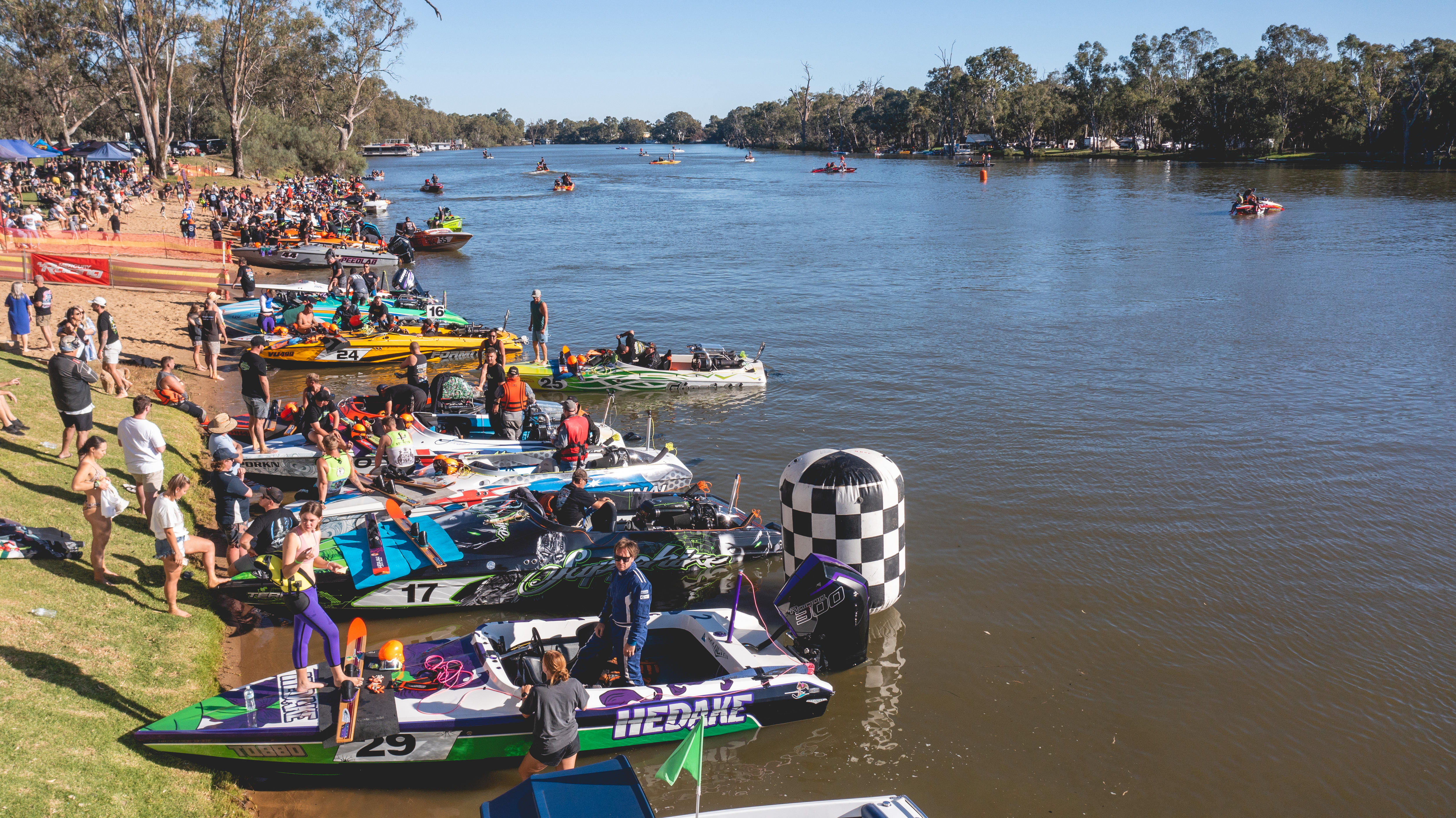 Barcos de esquí en la orilla del río, con algunos barcos en el agua al fondo
