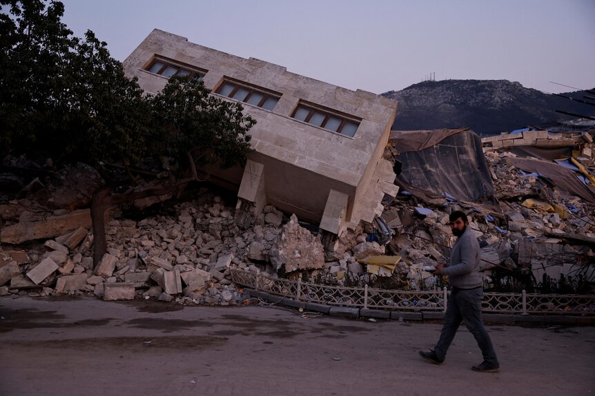 A man walks by a collapsed building and rubble caused by the earthquake in Antakya
