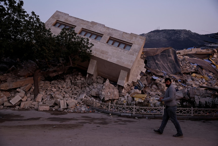 A man walks by a collapsed building and rubble caused by the earthquake in Antakya