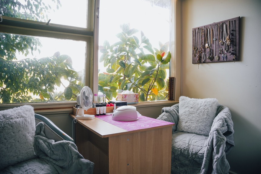 Deux chaises recouvertes de tapis sont assises près d'une fenêtre, une table avec des cosmétiques et du vernis à ongles entre elles.