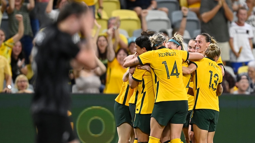 A group of Matildas players huddle together as a New Zealand player holds her hands to her head