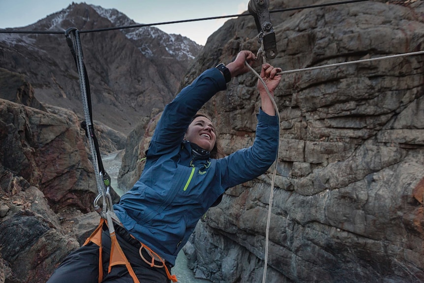 Dramatic rocky mountain landscape with adventurer Lucy Barnard on a wire repairing a cable