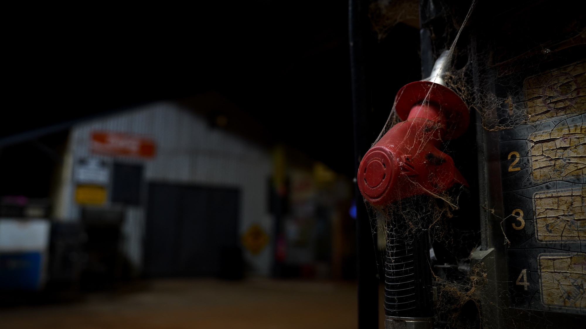 An eerie close-up photo of an old fuel pump's handle, which is covered in dust and cobwebs, taken at night time.