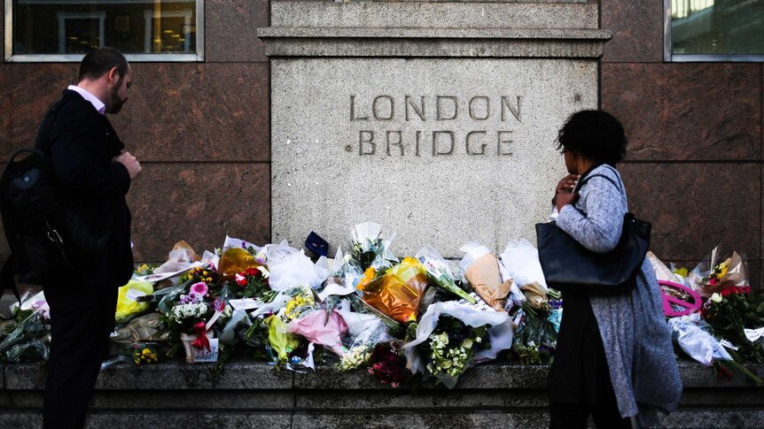 Two people stop to look at the collection of flowers left London Bridge terror attack victims