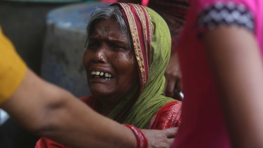 A close up of a woman crying, with a person reaching out to comfort her.