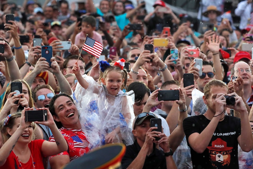 A little girl waving an American flag while crows around her take photos