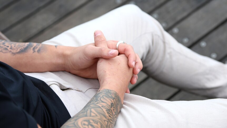 A man's hands are clasped in his lap.
