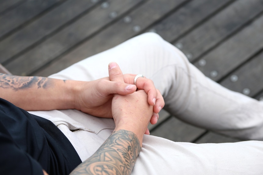 A man's hands are clasped in his lap.