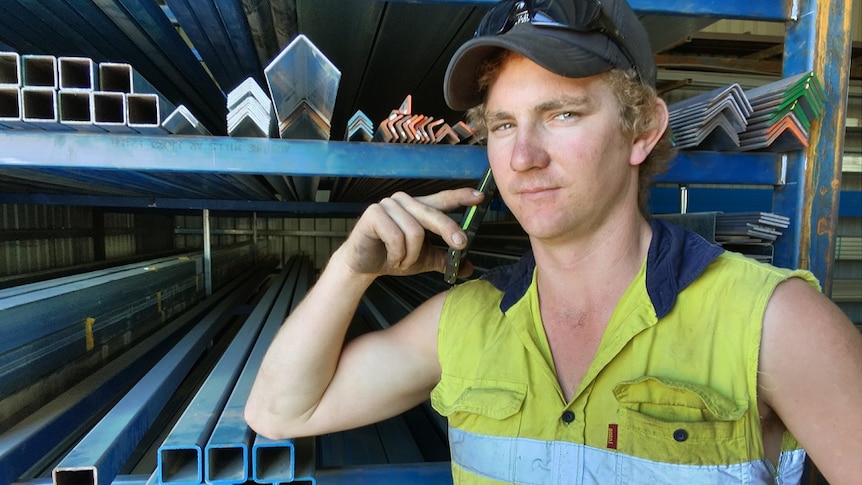 A young man stands in front of steel with a mobile phone to his ear